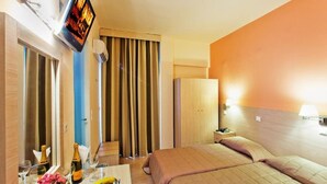 A hotel room with a bed, a TV mounted on the wall, a minibar, and a desk with a bottle of champagne and glasses. - Ambassador (Rhodes)