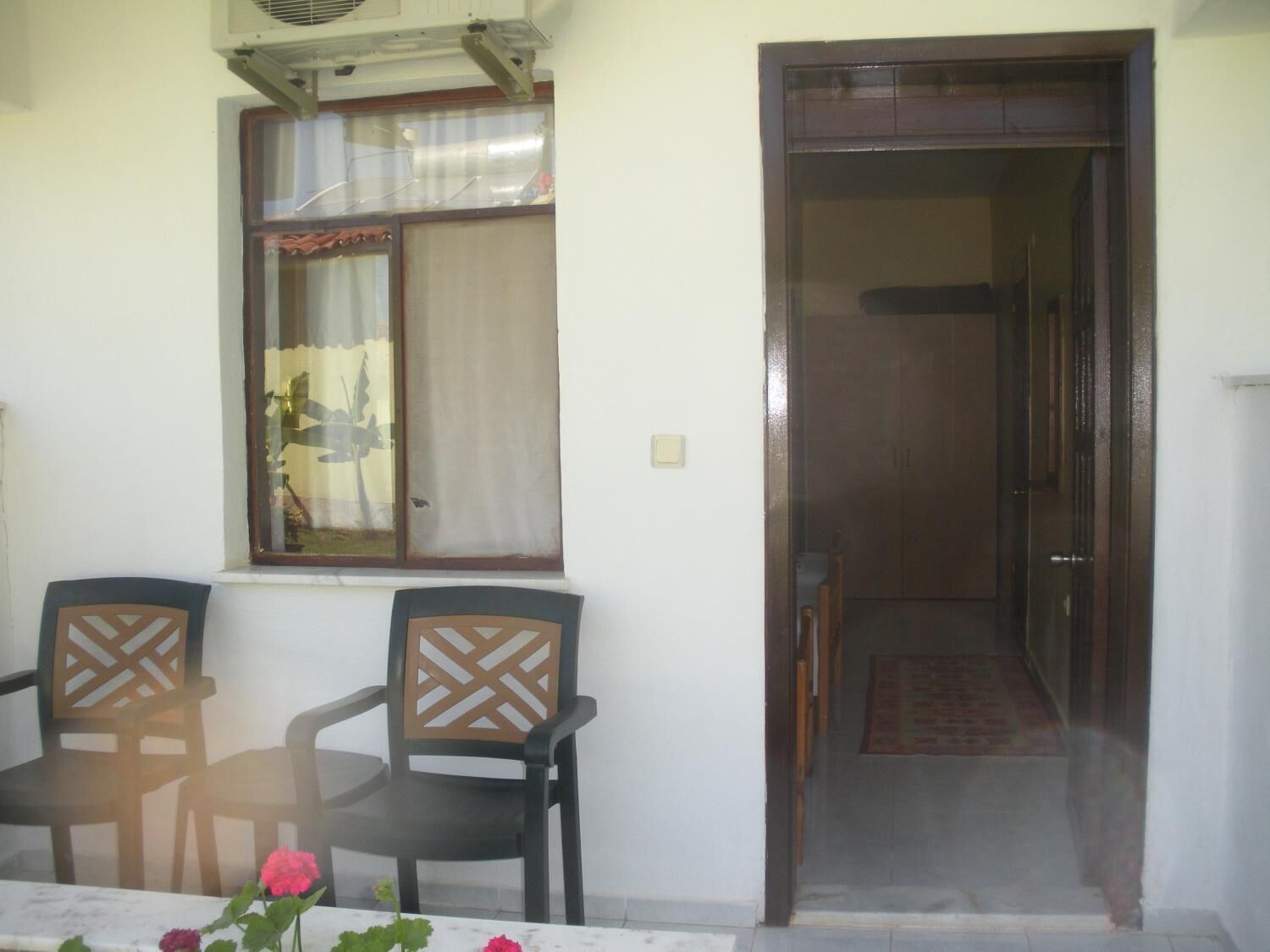 A room with two wooden chairs, a window with curtains, and a wooden door leading to a hallway.