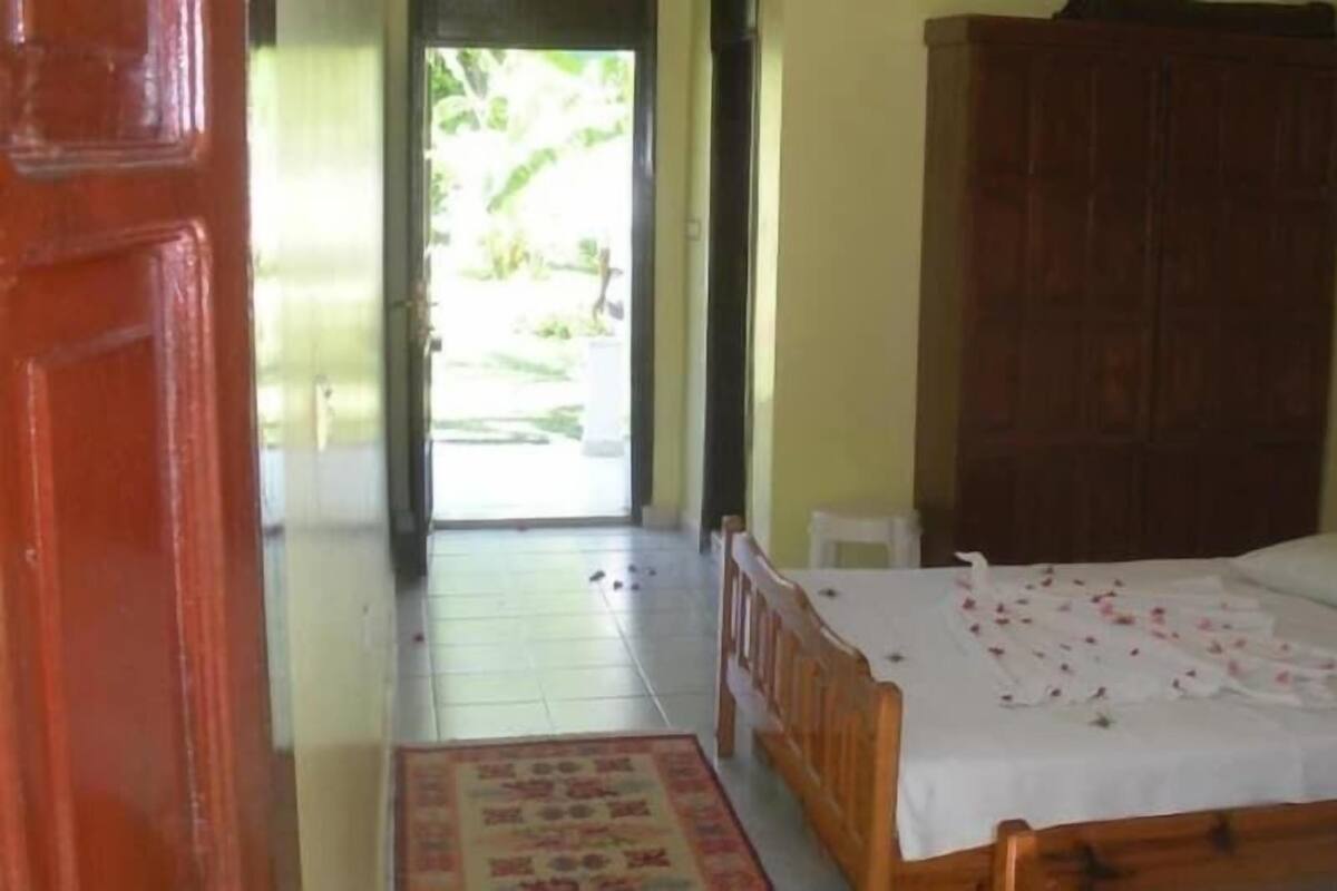 Un dormitorio con cama, armario de madera, suelo de baldosas y puerta que da a un balcón.