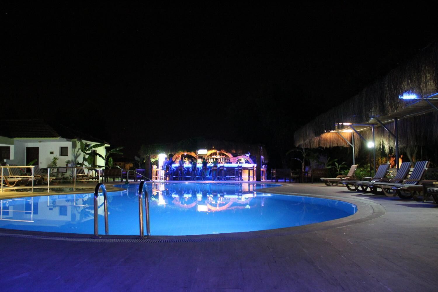 Zona de piscina nocturna amb gandules i zona de bar.