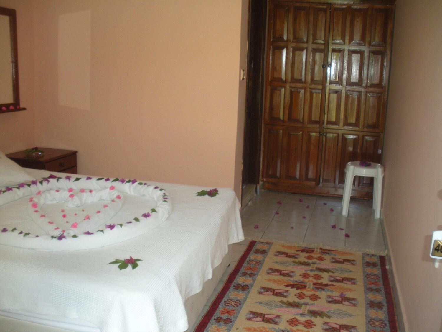 A hotel room with a bed, a nightstand, a wooden wardrobe, and a small stool.