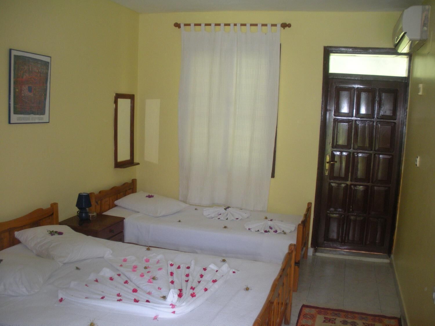 A room with two single beds, a wooden door, a mirror, and a framed picture on the wall.