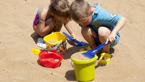 To børn leger med sand og legetøj på stranden.