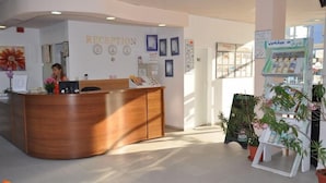 A reception area with a wooden reception desk, a clock, framed pictures, and a sign for workshops. - Hotel Belleville (Nessebar)