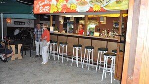 Un área de bar al aire libre con mostrador, taburetes y un tablero que anuncia comida y bebidas.