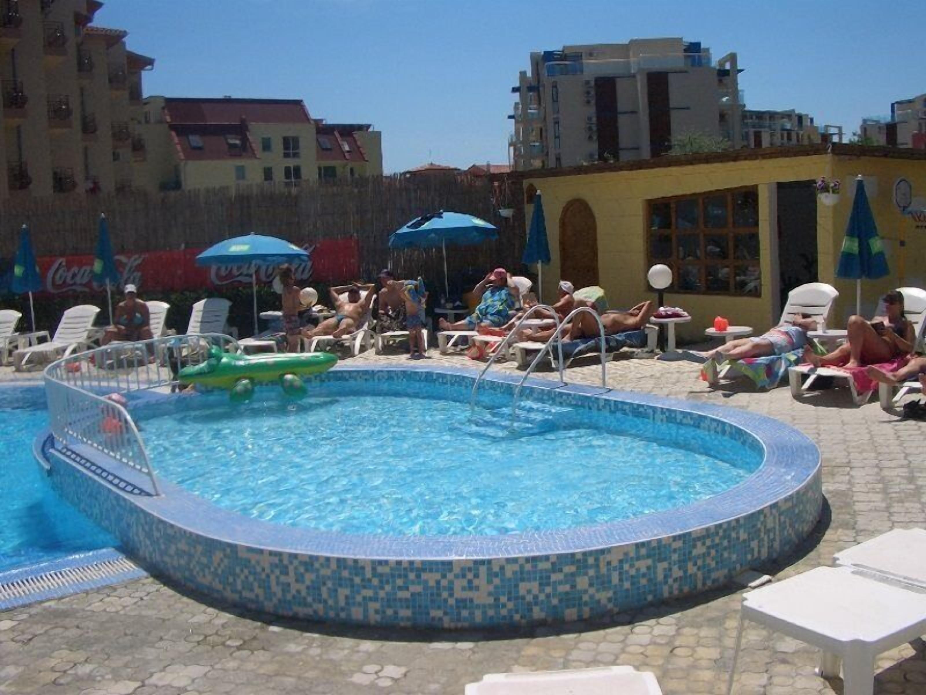 Una piscina con bordi piastrellati, circondata da lettini e ombrelloni.