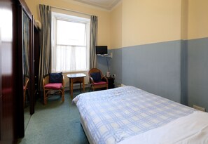 Een hotelkamer met een bed, twee stoelen, een tafeltje, een televisie en een raam met gordijnen.