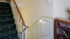 A staircase with green carpeted steps and white balustrades, leading to a landing with a bookshelf and framed pictures on the wall. - Fairways Hotel Paddington (London)