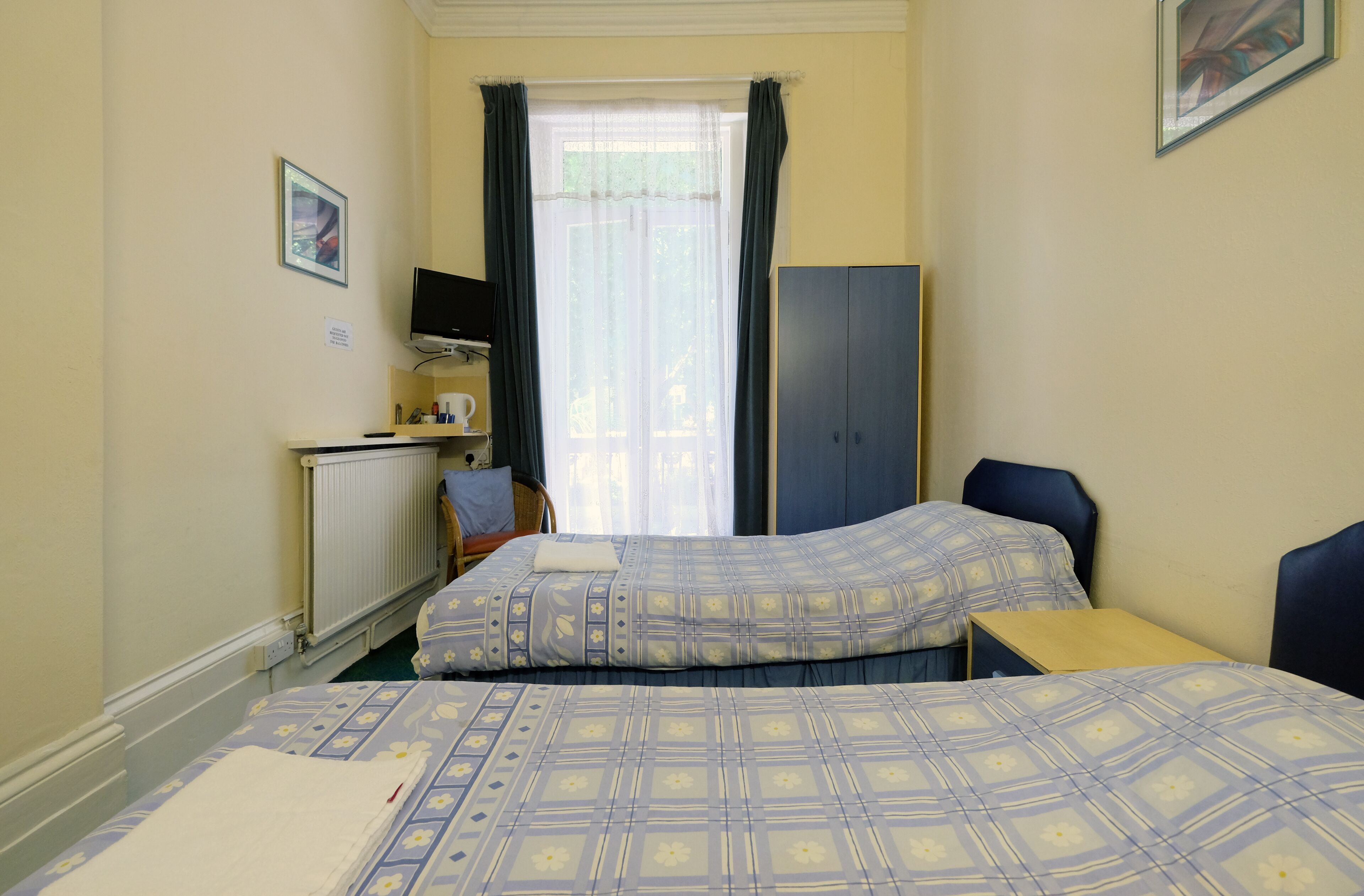 A hotel room with two beds, a desk, a chair, a wardrobe, a television, and a window with curtains.