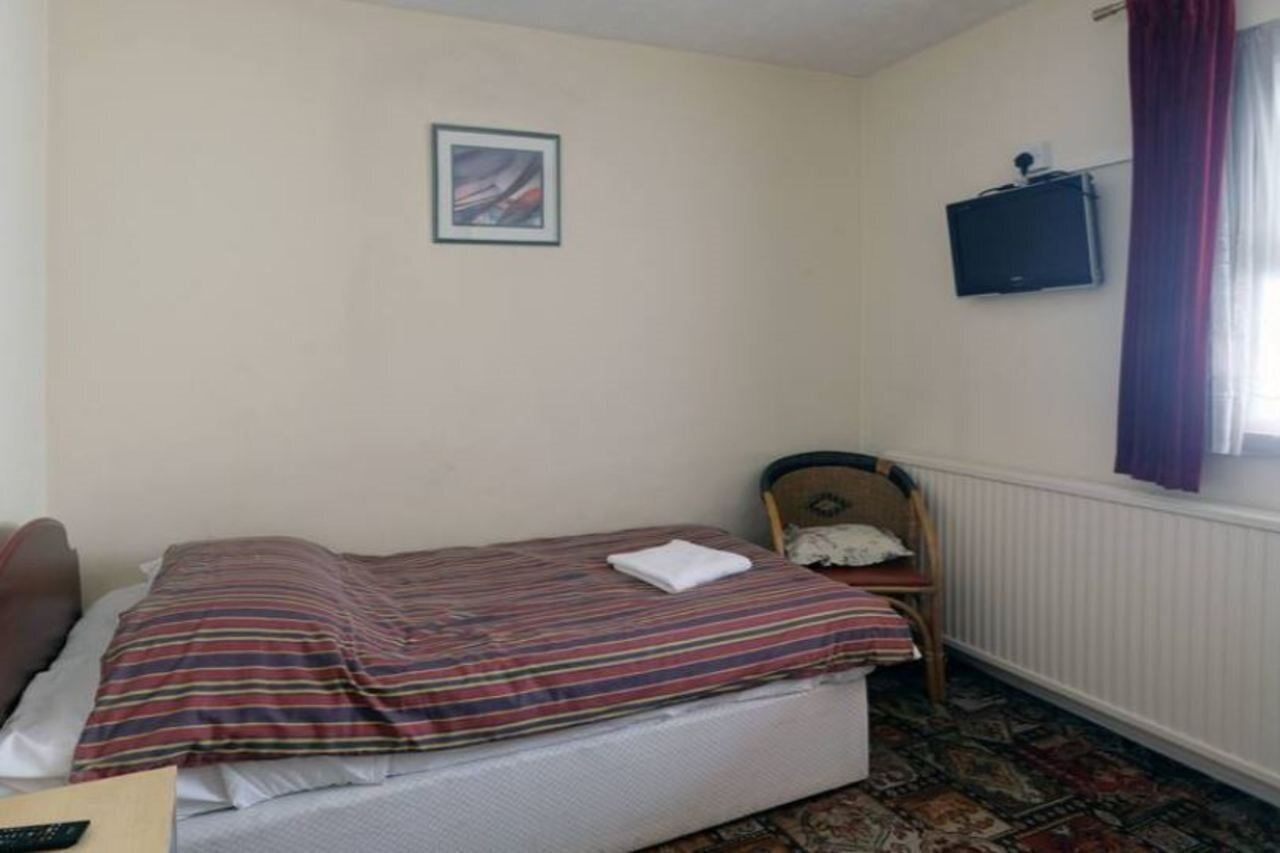 A small, simple room with a bed, a chair, a television, and a window with curtains.
