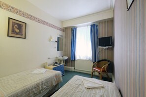 Een hotelkamer met twee éénpersoonsbedden, een klein bureau met stoel, een televisie en een raam met gordijnen.
