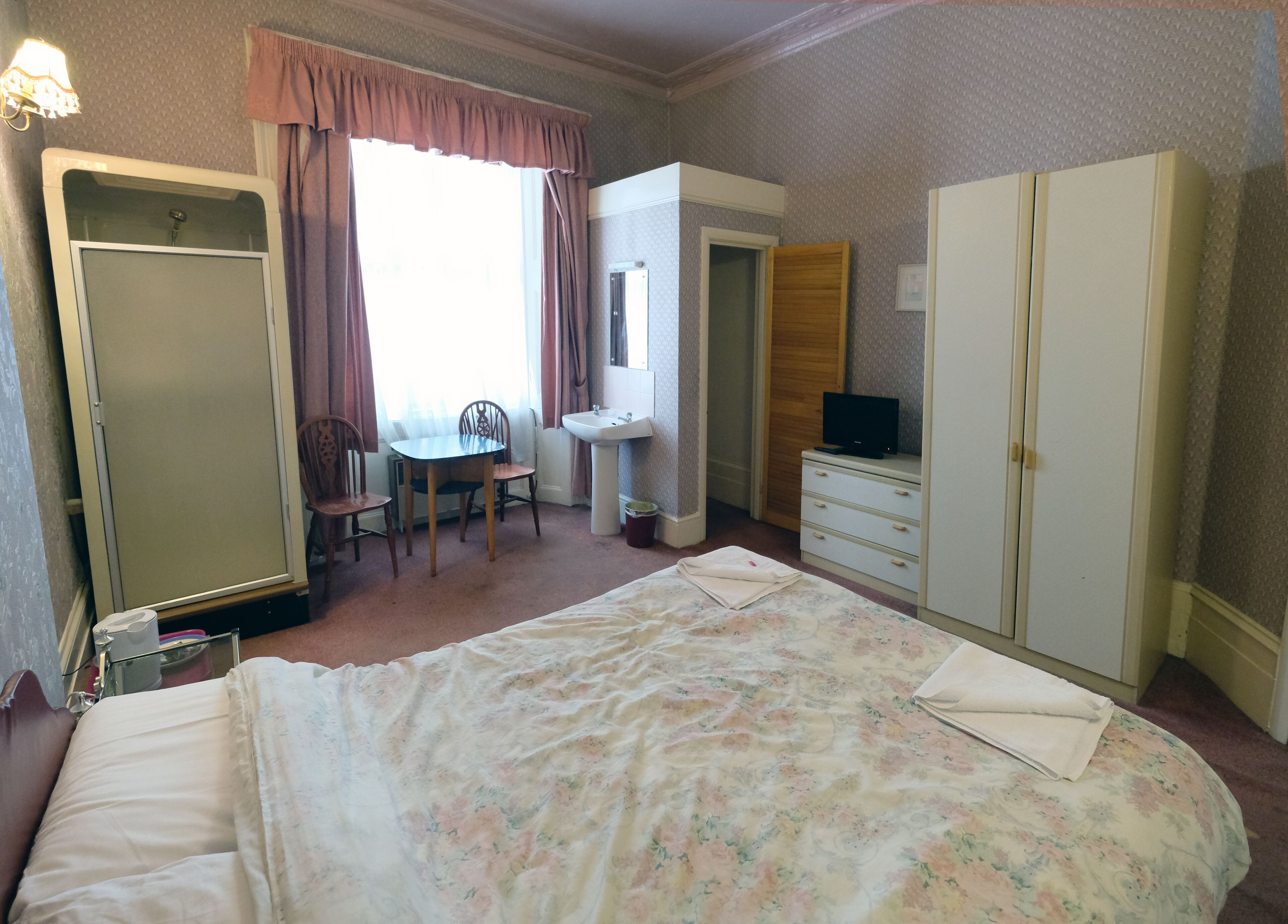 A bedroom with a bed, a desk, a chair, a wardrobe, and a bathroom.