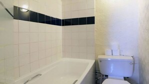 A bathroom with a bathtub, toilet, and a corner with a black tile accent. - Fairways Hotel Paddington (London)