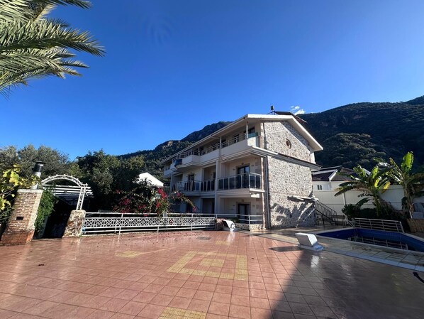 A two-story building with a stone facade and balconies, surrounded by a tiled patio and a pool area. - The Kumsal Hotel Ölüdeniz (Fethiye)