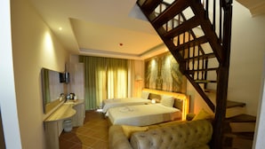 A hotel room with a wooden staircase, a sofa, two beds, a bathroom with a mirror and a sink, and a large painting on the wall. - The Kumsal Hotel Ölüdeniz (Fethiye)