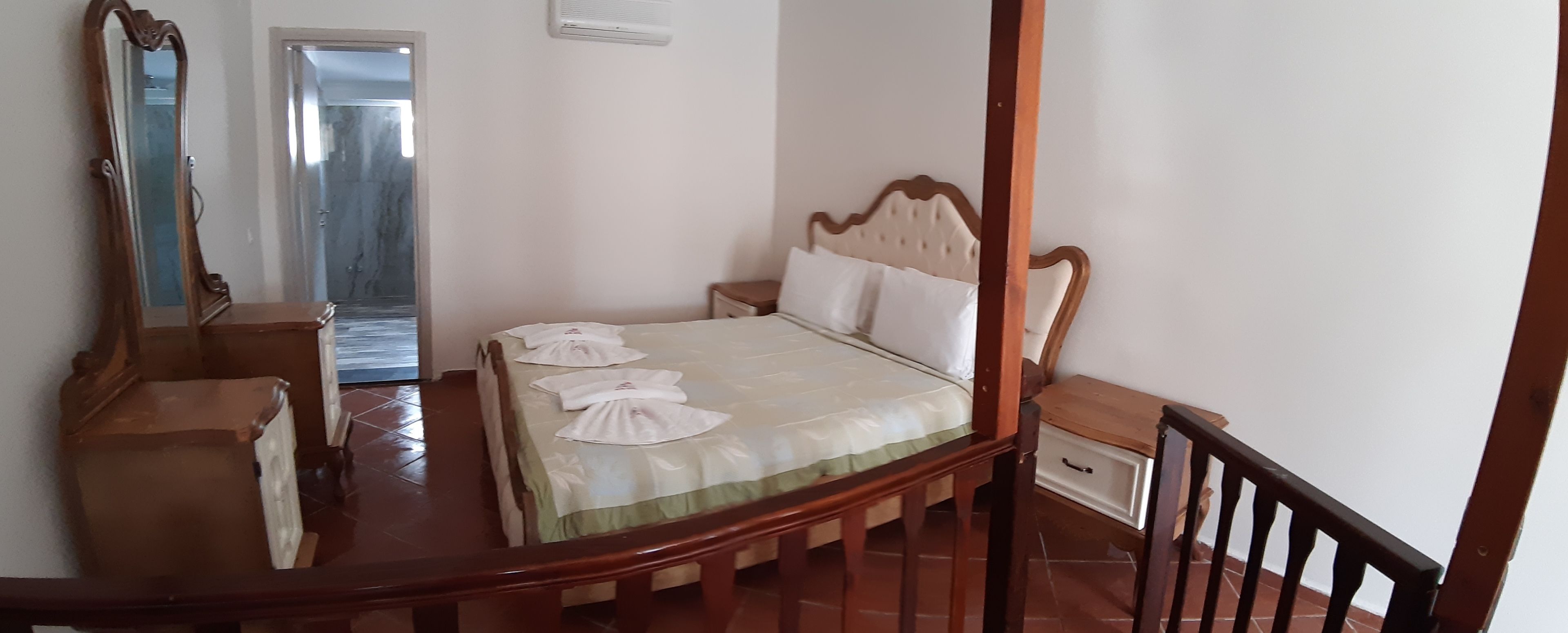 Ein Schlafzimmer mit einem hölzernen Bett, einem Nachttisch, einem Spiegel und einer Tür zum Balkon.