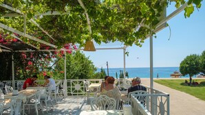 An outdoor cafe with white metal furniture, a pergola with hanging plants, and a view of the sea. - The Kumsal Hotel Ölüdeniz (Fethiye)