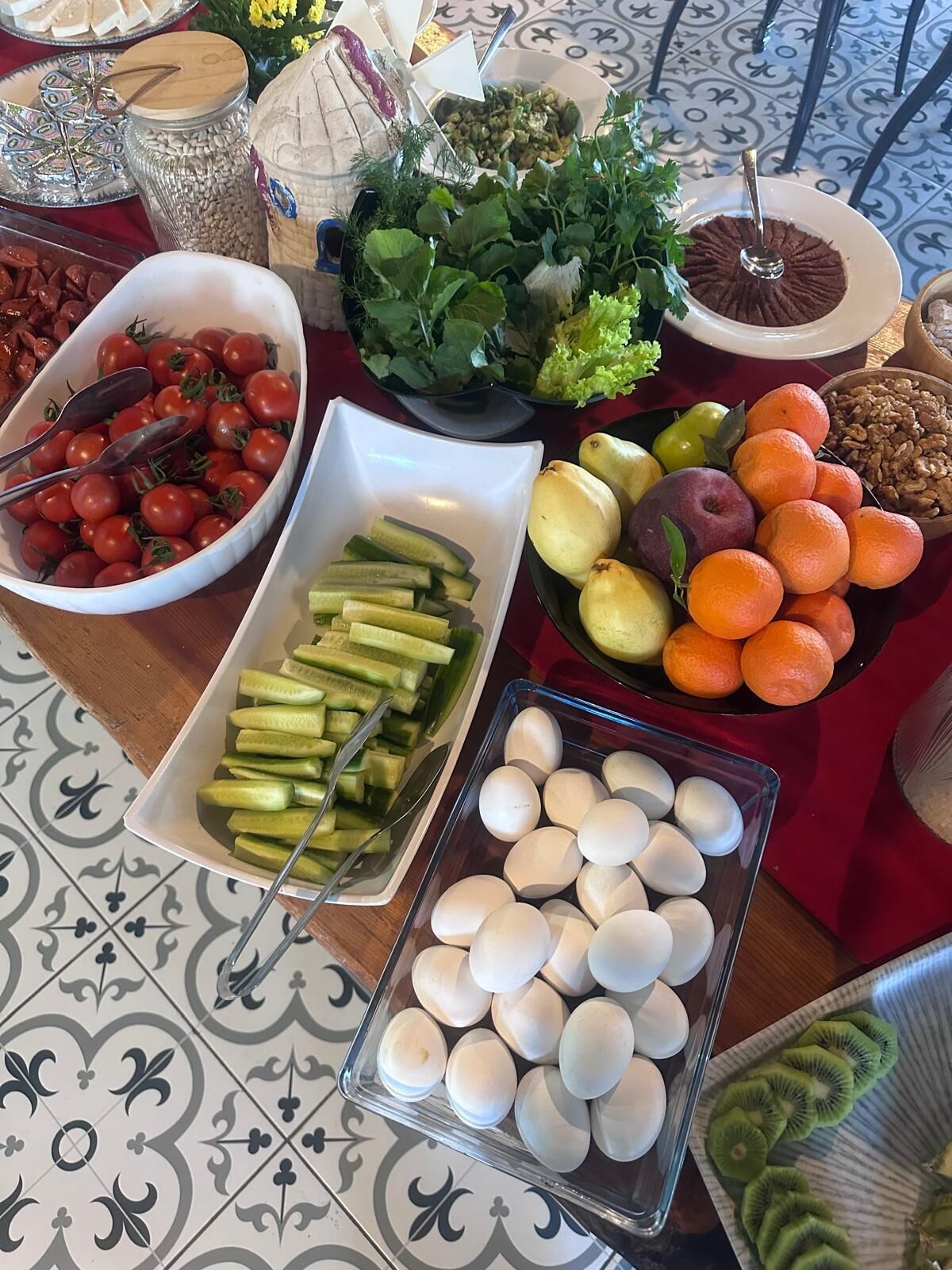 Une table de buffet proposant divers aliments, notamment des tomates, des concombres, des œufs, des oranges, ainsi que d’autres fruits et légumes.