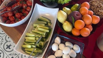 Une table de buffet proposant divers aliments, notamment des tomates, des concombres, des œufs, des oranges, ainsi que d’autres fruits et légumes.