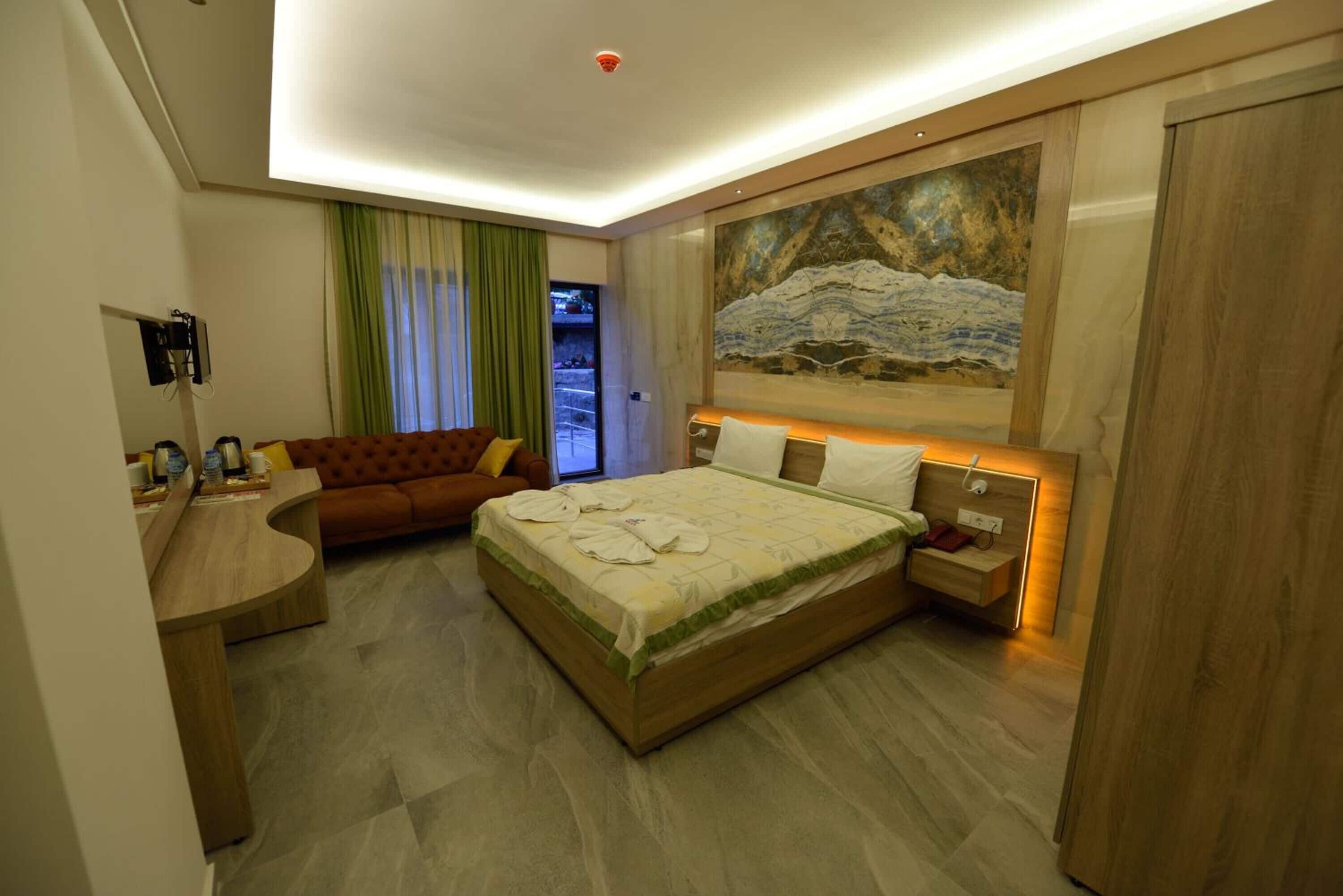 A modern hotel room with a bed, a sofa, a desk, and a painting on the wall.