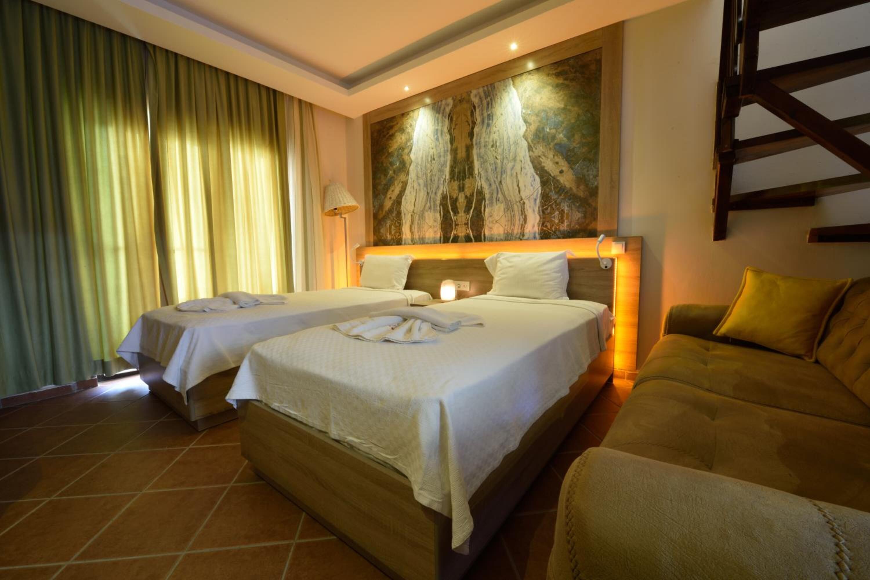 A hotel room with two beds, a large painting on the wall, a sofa, and a staircase.