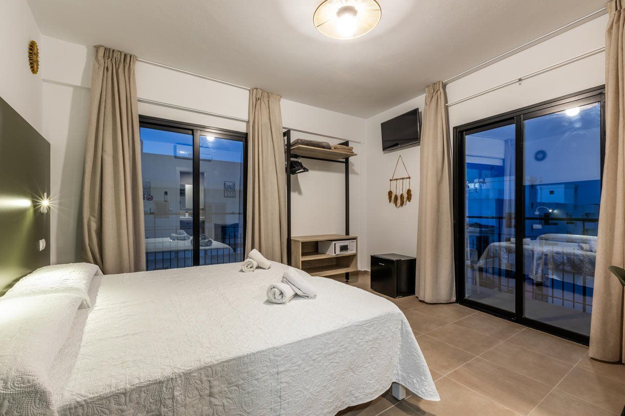 A hotel room with a bed, a desk, a TV, and a balcony with a view.