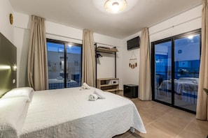 Une chambre d’hôtel avec un lit, un bureau, une télévision et un balcon offrant une vue.
