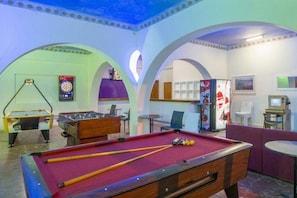 Una sala de billar con mesa de pool, mesa de futbolín, dardo y televisor.