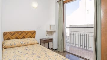 A bedroom with a bed, a nightstand, a wall-mounted light, and a view of a balcony.