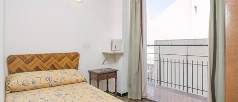 A bedroom with a bed, a nightstand, a wall-mounted light, and a view of a balcony.
