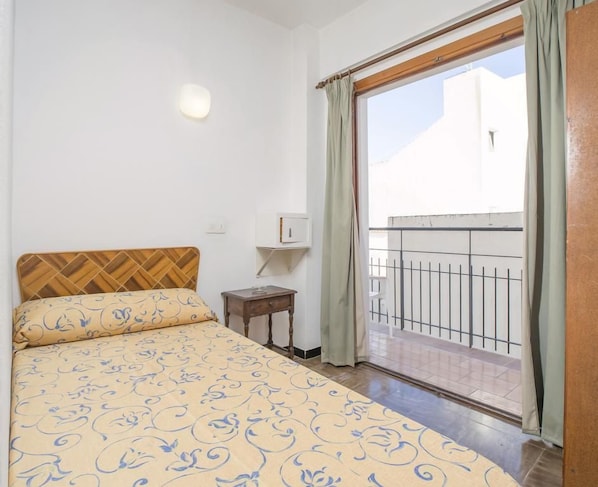 Un dormitorio con cama, mesita de noche, lámpara de pared y vistas a un balcón.