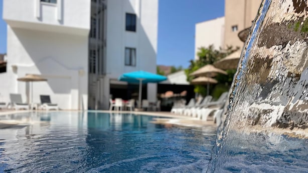 A swimming pool with a waterfall feature, lounge chairs, umbrellas, and a modern building in the background. - Eda Hotel (Marmaris)