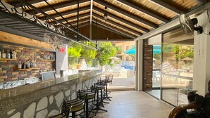 A covered outdoor bar area with a stone counter, multiple bar stools, and a view of the outdoor seating area. - Eda Hotel (Marmaris)