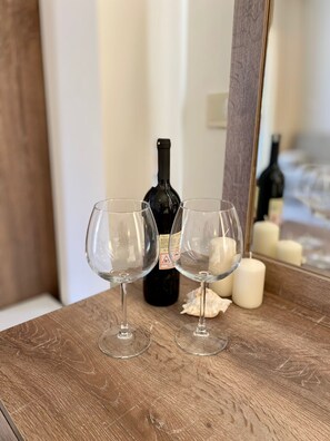Two empty wine glasses on a wooden surface with a wine bottle and candles in the background. - Eda Hotel (Marmaris)