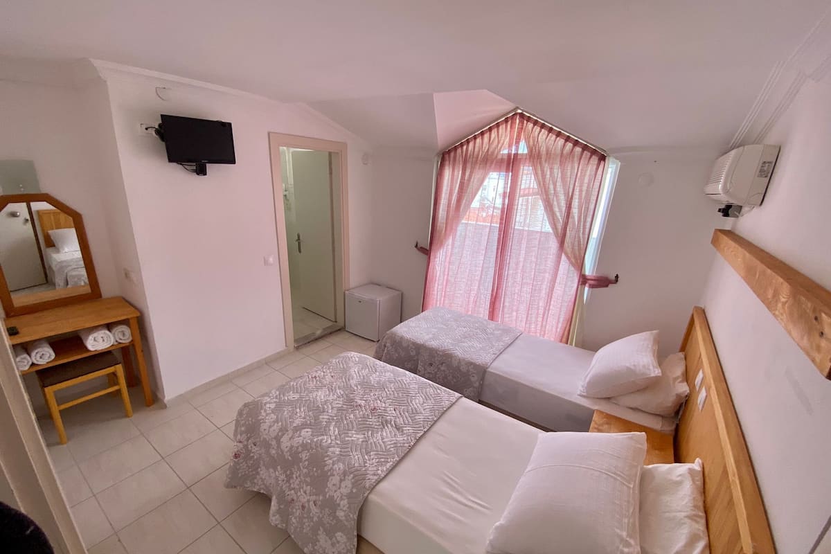 A bedroom with two beds, a mirror, a TV, and a small table with towels.