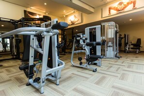 A gym with various exercise machines, a mirrored wall, and a wooden floor.