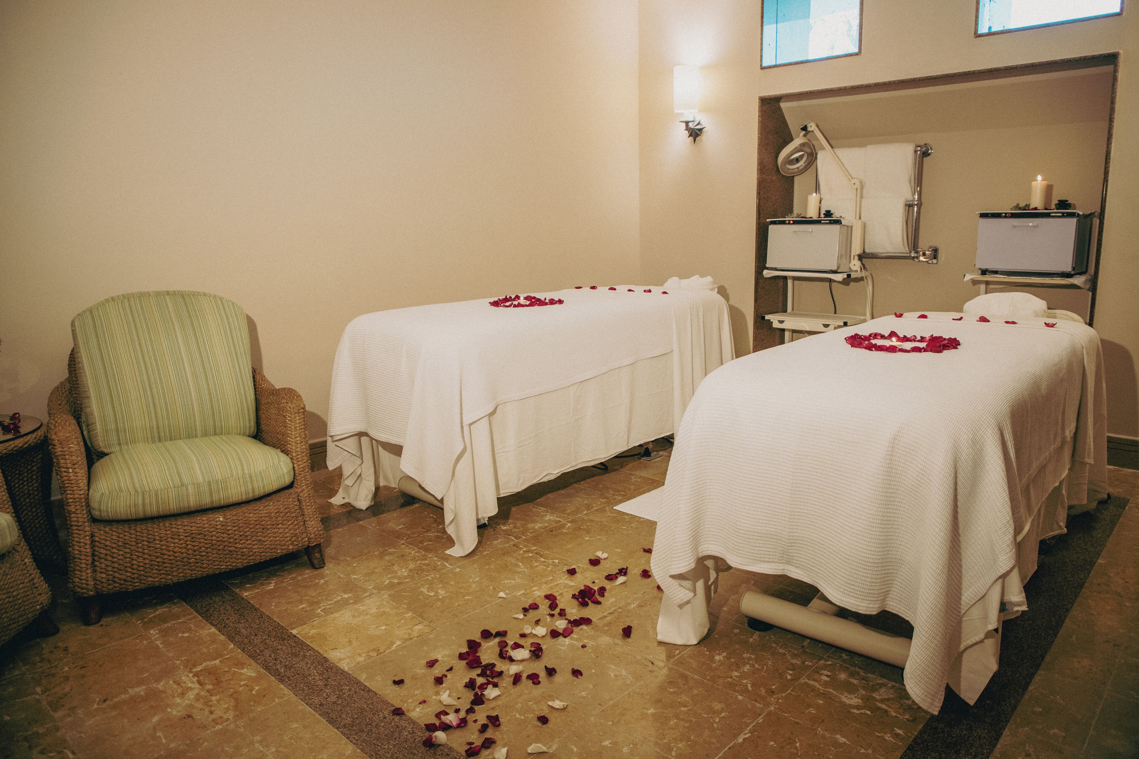 A spa room with two beds, a green chair, and a massage table.