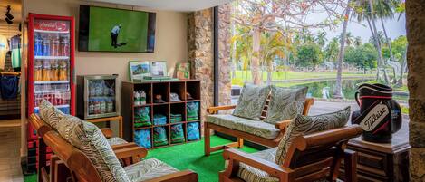 Una habitación con muebles de madera, televisión, refrigerador Coca-Cola y vista a un campo de golf.