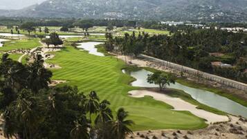 Campo de golf con búnkeres de arena, obstáculos acuáticos y palmeras.