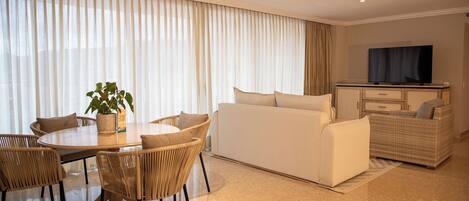 A modern living room with a dining area, a sofa set, a television, and a wicker chair.