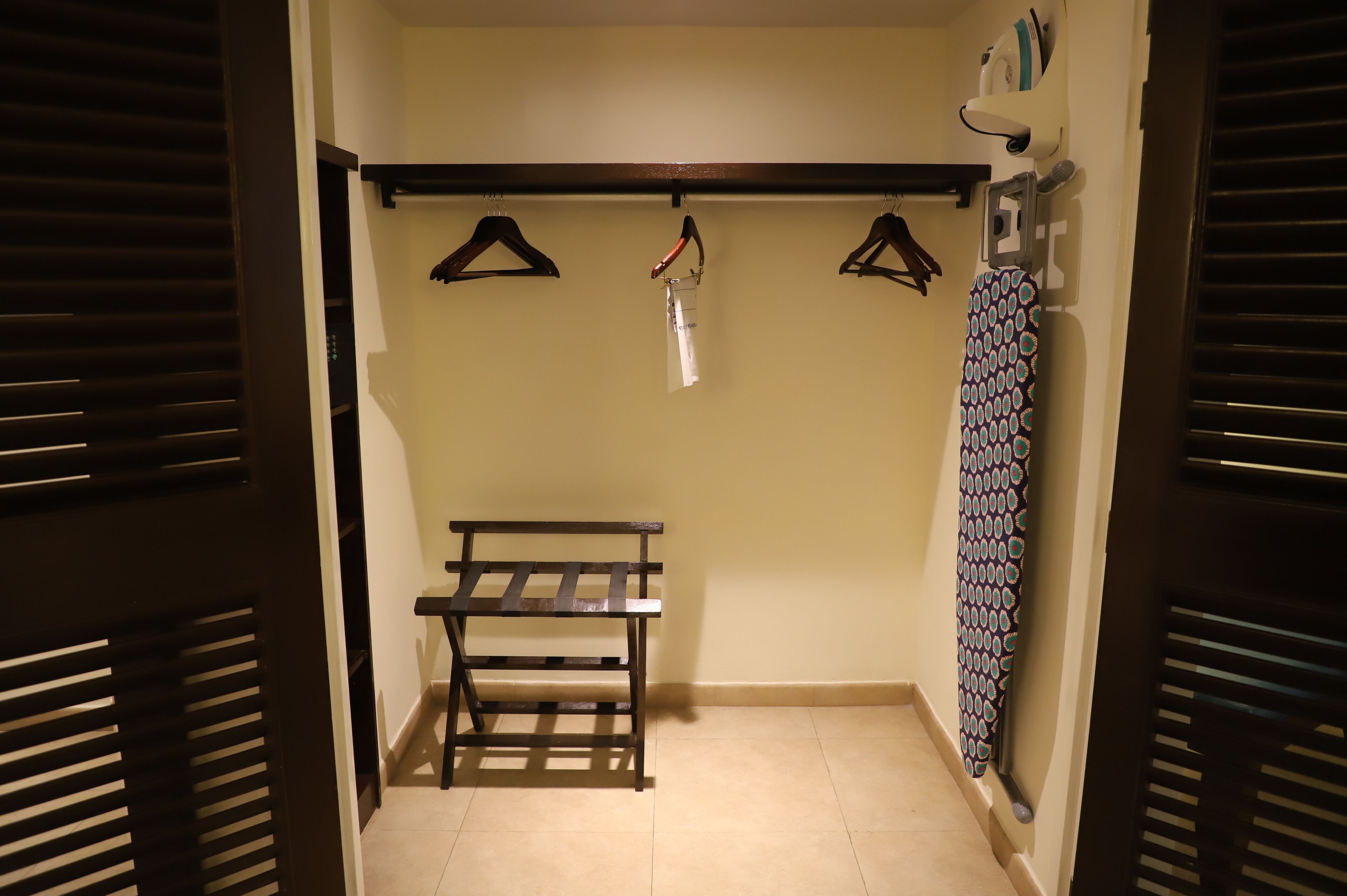 A closet with a bench, a hanging rack, and a patterned item on the wall.