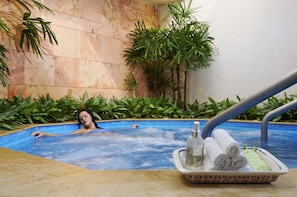 A person relaxing in a hot tub surrounded by lush green plants.