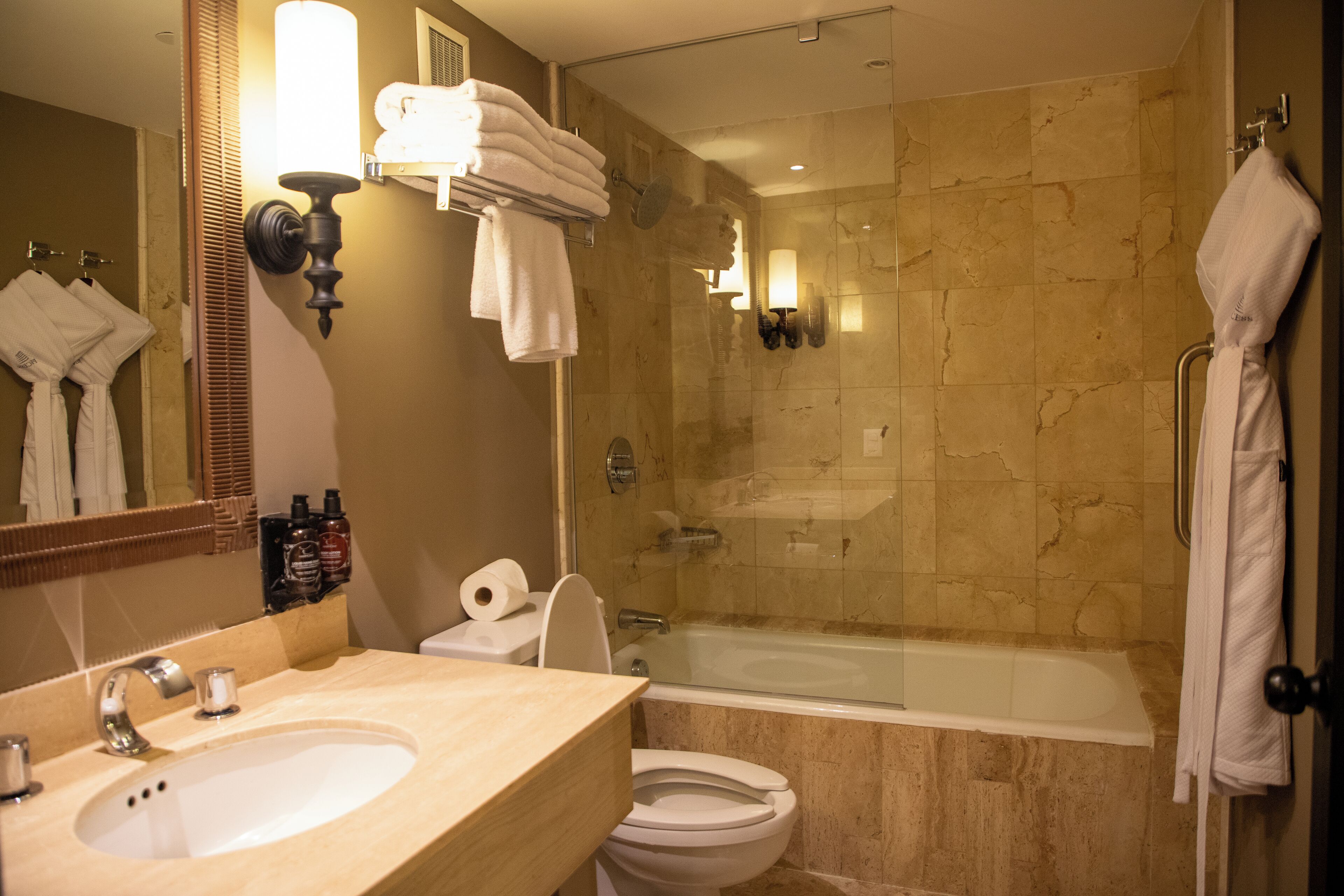 Un baño con lavamanos, inodoro y bañera. Hay toallas colgadas en la pared y un espejo sobre el lavamanos.