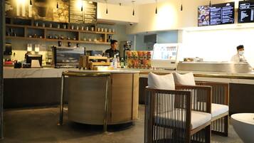 Interior moderno de un café con barra, mesas y una pantalla digital con el menú.