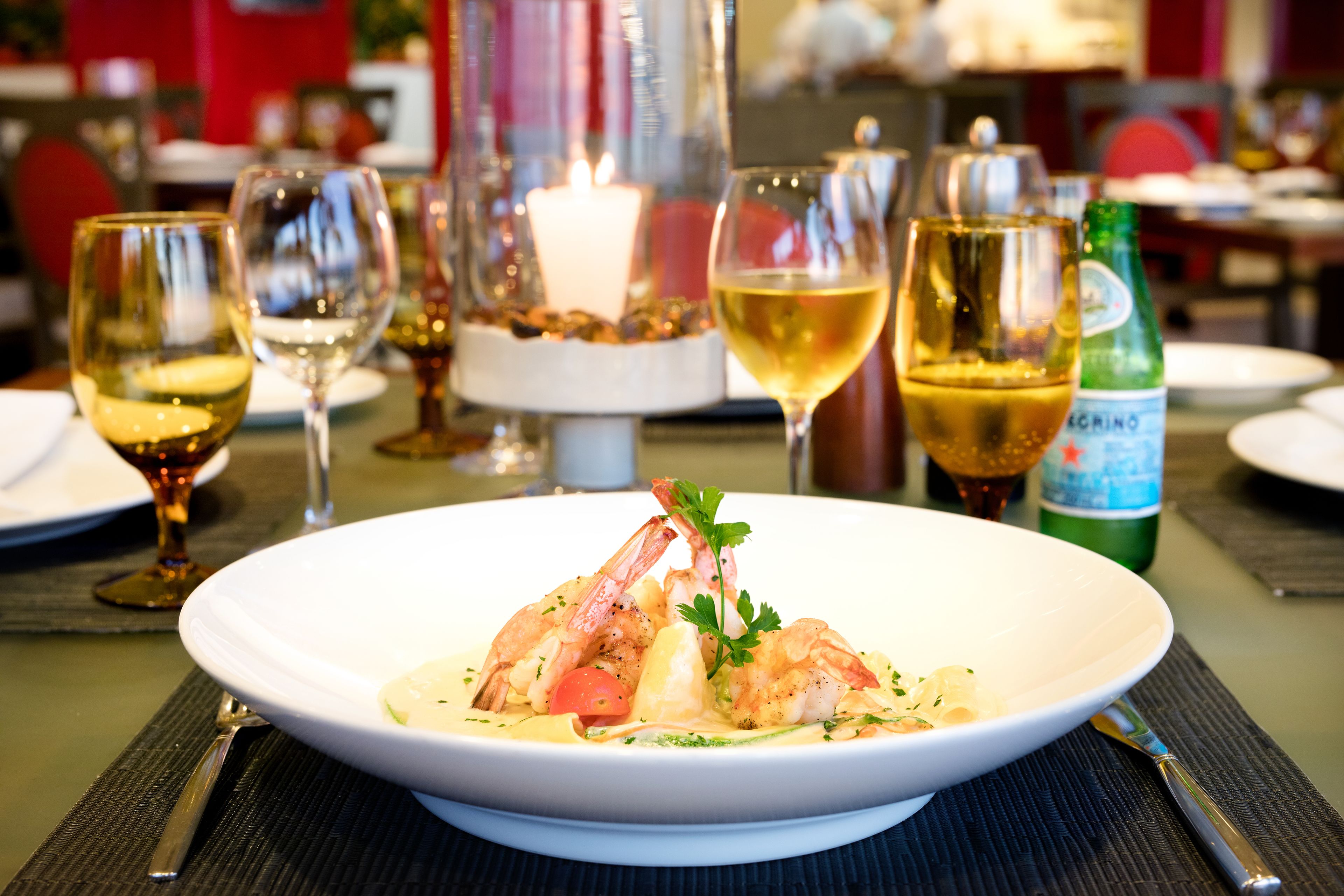 A dining table with a white plate of seafood, wine glasses, and a candle.