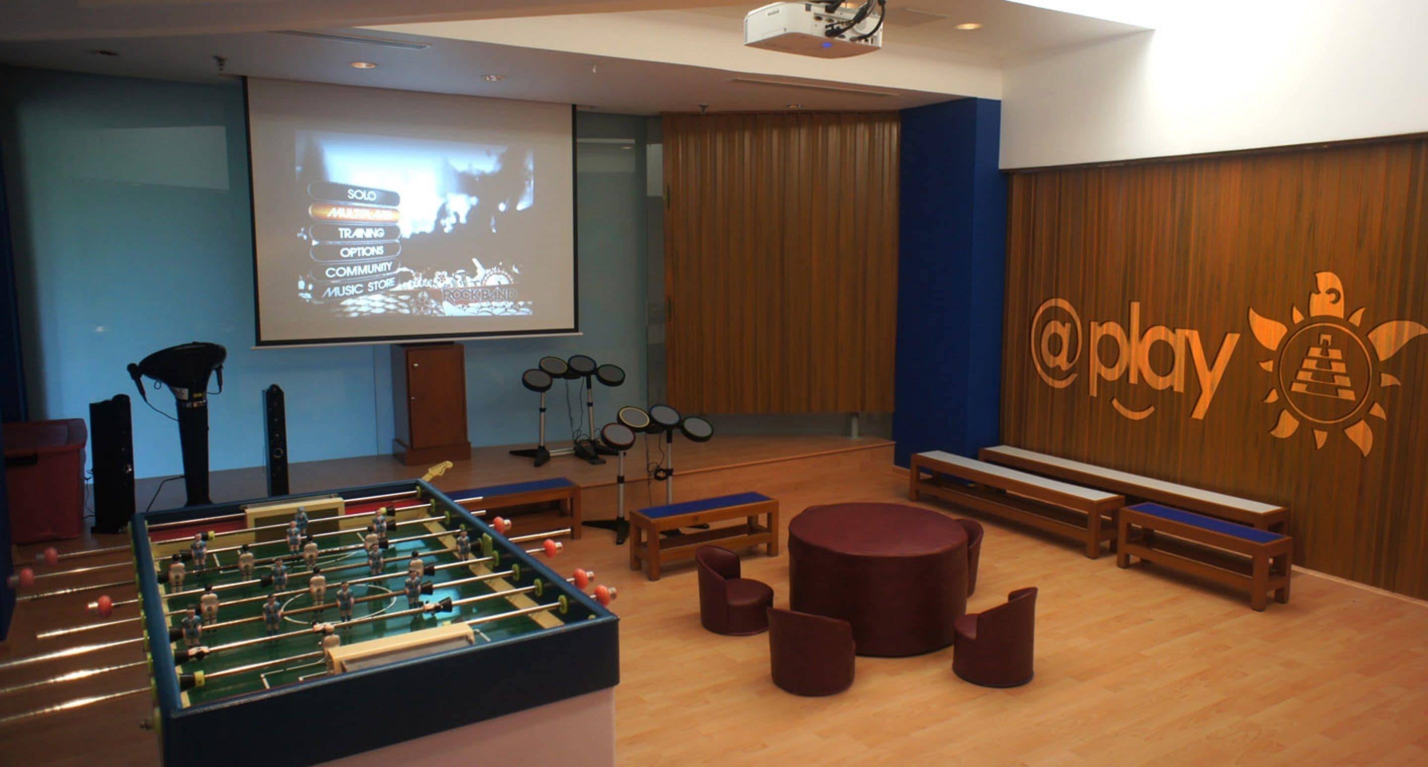 A room with a foosball table, a projection screen, and a logo on the wall.