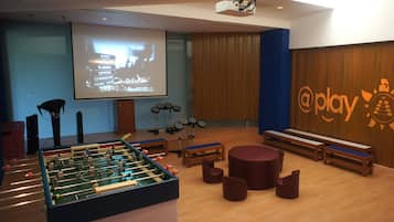 Een kamer met een tafelvoetbaltafel, een projectiescherm en een logo op de muur.
