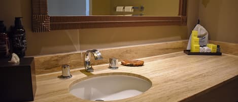A bathroom with a marble sink, a mirror, and toiletries on the counter.
