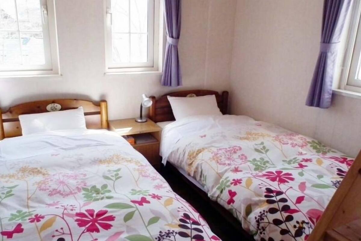 Ein Zimmer mit zwei Einzelbetten, jeweils mit Blumenmuster-Bettdecke, Holz-Kopfseitenverkleidung und einem Nachttisch mit Lampe.