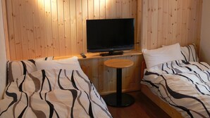A room with wooden panel walls, a television on a stand, two beds with striped bedding, and a small round table. - Pension Locomotion (Kutchan)